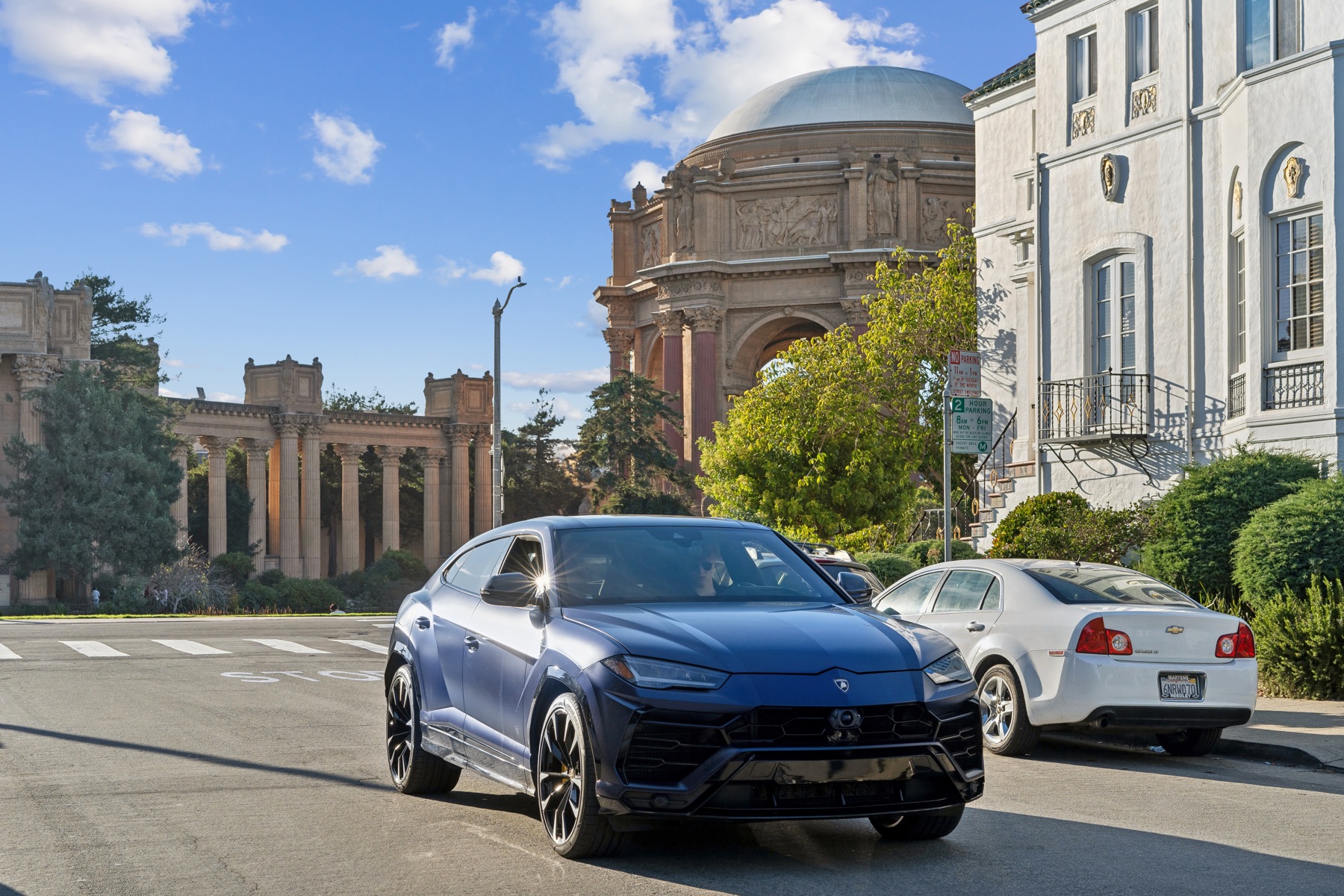 A blue Lamborghini Urus passing the Palace of Fine Arts in afternoon light